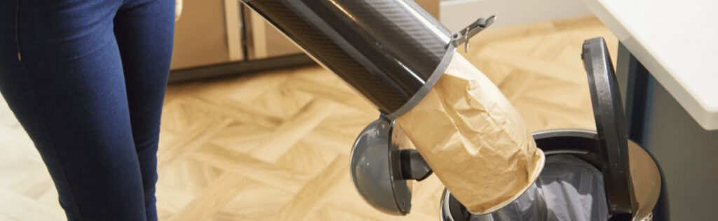 Person sealing a vacuum bag and desposing of it in a trash can.